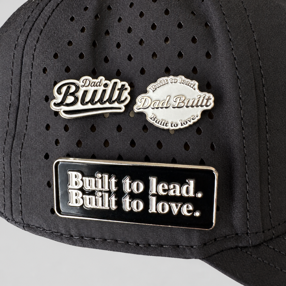 Dad Built three-pin set displayed on a black perforated cap against a studio-gray background